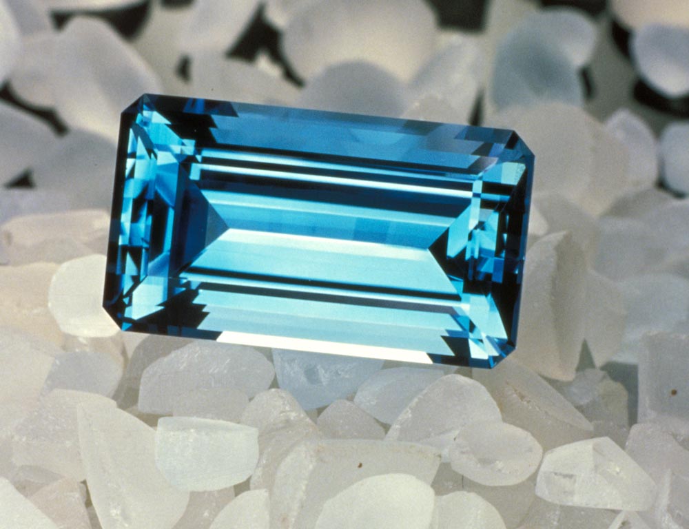 Single, faceted irradiated Topaz (blue), nested atop a series of rough Topaz.